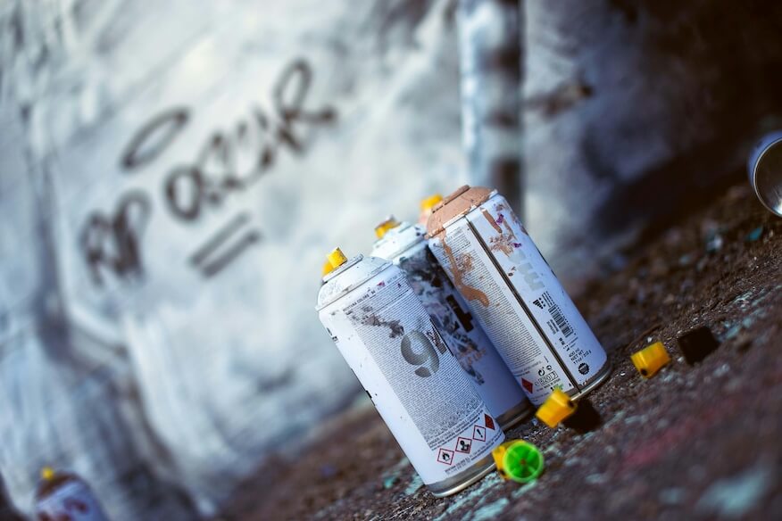 Mehrere leere oder gebrauchte Graffiti-Sprühdosen liegen neben bunten Caps auf dem Boden.