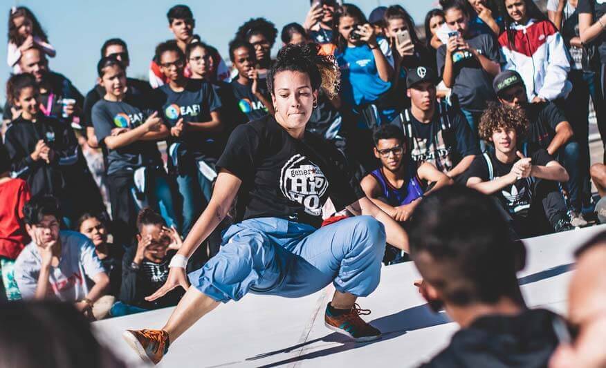 Szene aus der Hip-Hop-Kultur, die einen Breakdancer in der Pose des „freezing“ vor einer Gruppe von Zuschauern zeigt, als visuelle Darstellung der Verbindung von Graffiti und Tanz.