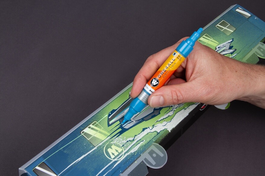 Eine Hand hält einen Molotow ONE4ALL Marker und zeichnet präzise Details auf ein Graffiti-Stück.